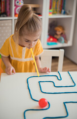 Little girl enjoying game playdough straw maze. Great activity for building oral motor skills at home.