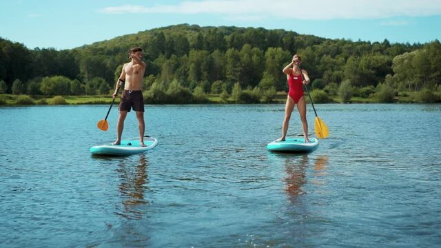 Happy man and woman in a bathing suit standing on sup board and swims surfing on the lake with a paddle for swimming rowing sport surfer friends close up slow motion