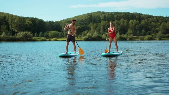 Young man and woman in a bathing suit standing on sup board and swims surfing on the lake with a paddle for swimming rowing sport surfer friends close up slow motion