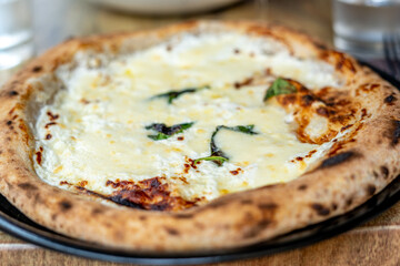 Pizza five cheeses with spinach on black plate on wooden table. Selective focus. Macro close-up
