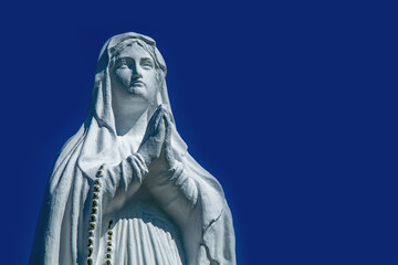 Virgin Mary ancient statue against blue background of sky.