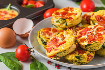 Fototapeta na wymiar Keto or low carb diet breakfast. Egg cups or omelet with spinach and tomatoes in a plate and muffin cups
