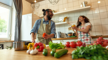 Italian cook looking at his girlfriend while preparing vegetables for cooking healthy meal, young woman smiling, helping him in the kitchen