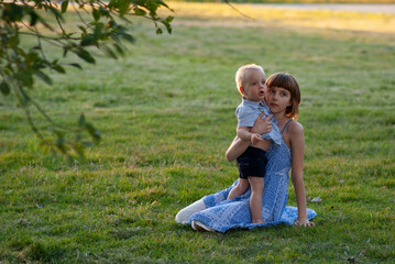 Naklejka na ściany i meble Girl with her little brother are sitting in a clearing in the park