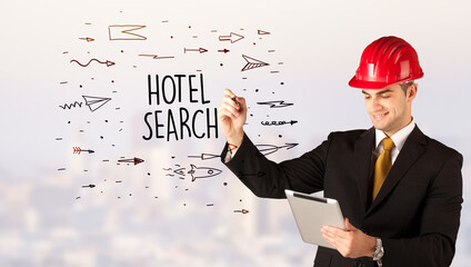 Handsome businessman with helmet drawing HOTEL SEARCH inscription, contruction sale concept