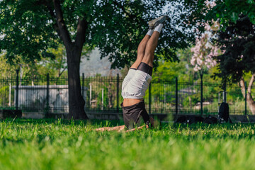 Young sporty handsome man practicing yoga in the park and doing the plow pose..