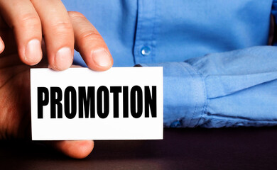 PROMOTION is written on a white business card in a man's hand. Advertising concept