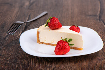 Slice of cheesecake with strawberries on a white plate over wooden background.