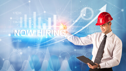 Young businessman with helmet drawing NOW HIRING inscription, modern business technology concept