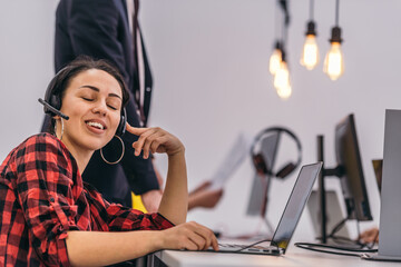 Portrait of a beautiful young woman wearing headset and  smiling while working on the laptop
