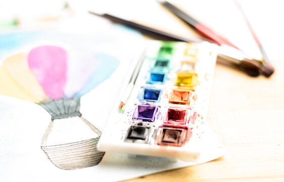watercolor paint palette.
paint palette and paintbrushes and a watercolor painting on paper