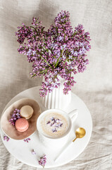 Cappuccino with macaroons on linen tablecloth, violet lilac flowers, morning concept