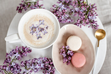 Fototapeta na wymiar Cappuccino with macaroons on linen tablecloth, violet lilac flowers, morning concept