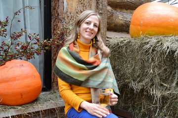Happy woman with a mug of tea in her hand sits against the background of orange pumpkins in the...