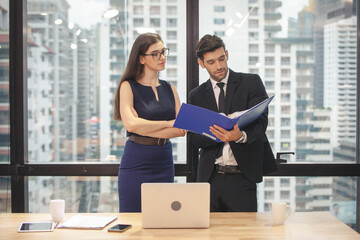 Businessman and businesswoman using a laptop together while standing in front of office building windows overlooking the city. confident businesspeople using a laptop working in a modern office