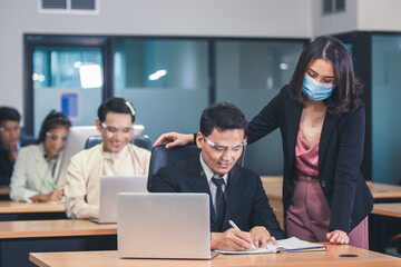 young business with face mask work plan in the office. Businessman and businesswoman using a laptop together while standing in front of office