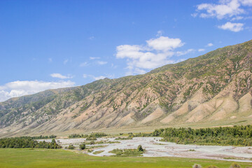 Rural landscape: blue cloudy sky, mountains, small river and a distant village. August, Kazakhstan