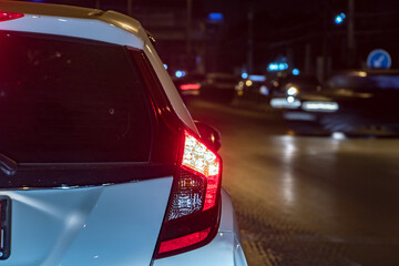 A tail-light of car at night city. A red light at the rear of a white car waiting at crossroad.