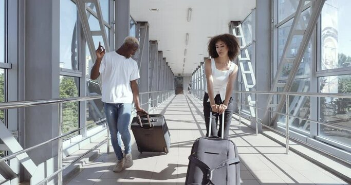 Couple of foreign students happy to arrive in new city, African American guy and curly ethnic woman dancing at airport terminal choreography with luggage, carried pushing suitcases synchronously