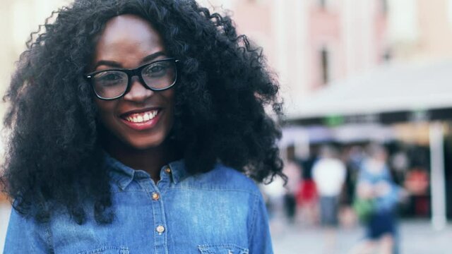 Close up portrait of young happy exchange student with lush curly hair. Beautiful girl in denim shirt waving British flag on street.