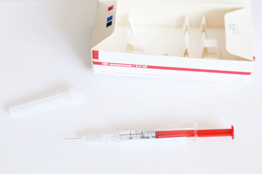 Used dose of Interferon injectable solution in pre-filled syringe for the treatment of Hepatitis C, next to plastic cap and carton box. Text translation: '180 micrograms'