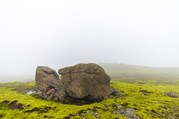 big stone in the middle of a green grass field on a very foggy day