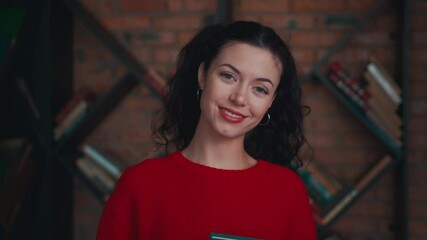 young curly female staying with book and looking at camera