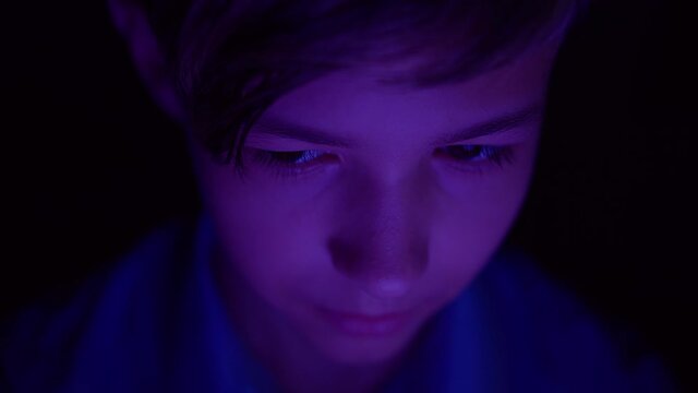 portrait of a boy playing a computer game on the tablet at night