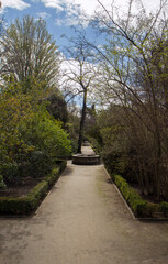 Empty park in a sunny day. Serene atmosphere. The footpath along the garden, leading to a concrete fountain. 