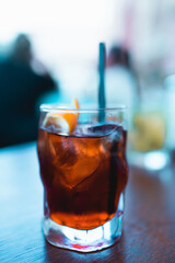 Negroni cocktail close up in the outdoor tables of a bar. Orange and red alcohol, orange peel, ice cubes. Italian aperitif for mature and expert drinkers.