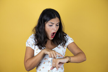 Obraz premium Beautiful woman over yellow background surprised and pointing his watch because it's late