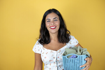 Beautiful woman over yellow background doing housework holding a basket with clothes