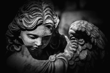 Death. Close up sad angel as symbol of pain, fear and end of life. Ancient stone statue. Black and white background.