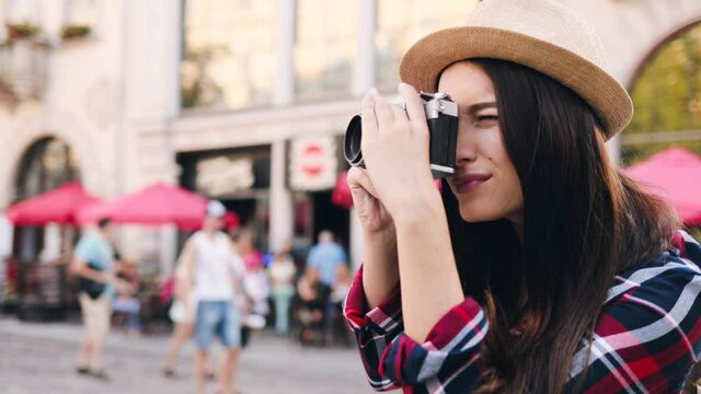 Portrait of young tourist girl makes photo of architecture on old camera. Attractive woman traveling alone and enjoys her hobby.