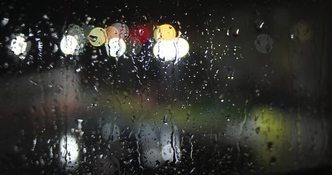 Timelapse video of drops of night rain on the window and blurred backlight