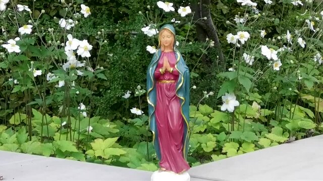 Maria Statuette vor wei&szlig;en Blumen im Wind, mit betenden H&auml;nden, voll der Gnade und Demut