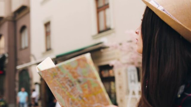 Close up of camera spinning around tourist girl with paper map in hands standing in the middle of street.