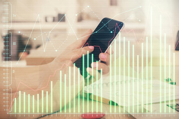 Double exposure of man's hands holding and using a digital device and forex graph drawing. Financial market concept.