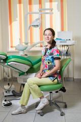 Portrait of young female dentist on dental chair next to dental dashboard