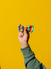 Male hand hold LGBT colors bow tie on yellow background