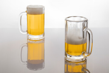 Beer mugs with beer. Beer without frosting. Beer mugs on white backlit background. One glass almost empty and one full.