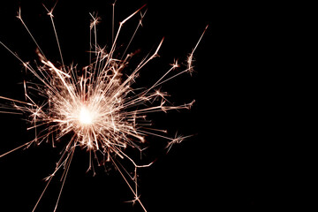 A closeup of a sparkler burning fiercely. Detailed sparks fly in all directions. Black background.