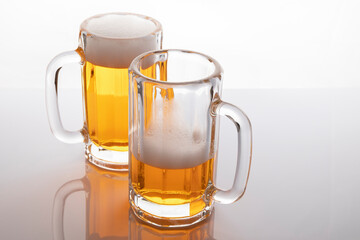Beer mugs with beer. Beer without frosting. Beer mugs on white backlit background. One glass almost empty and one full.