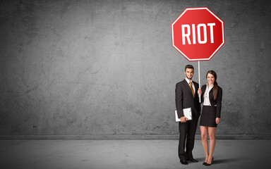 Young business person holding road sign with RIOT inscription, new rules concept