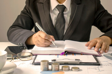 Close-up of a man writing financial notes on his desk, including financial and accounting documents.