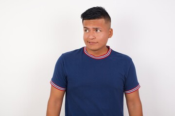 Photo of amazed Young handsome hispanic man wearing casual t-shirt standing over white isolated background bitting lip and looking up to empty space,