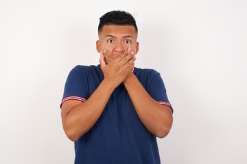 Young handsome hispanic man wearing casual t-shirt standing over white isolated background shocked covering mouth with hands for mistake. Secret concept.