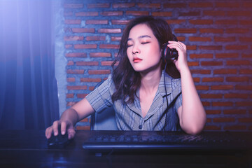 Asian Gamer girl woman nerdy geek casual playing video games computer cheering winning having fun excited at home computer desk setup technology wearing headset voice chat team play online cyberspace