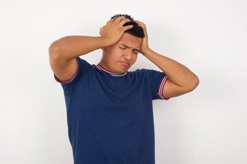 Young handsome hispanic man wearing casual t-shirt standing over white isolated background suffering from strong headache desperate and stressed because of overwork. Depression and pain concept.