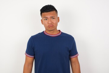 Portrait of displeased upset Young handsome hispanic man wearing casual t-shirt standing over white isolated wall frowns face as going to cry, being discontent and unhappy as can't achieve goals,  